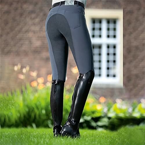 Person wearing equestrian breeches and boots, standing outdoors.