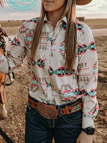 Person wearing a patterned western shirt and jeans next to a horse.