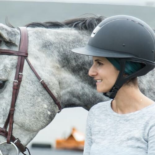 Woman wearing a helmet standing next to a horse.